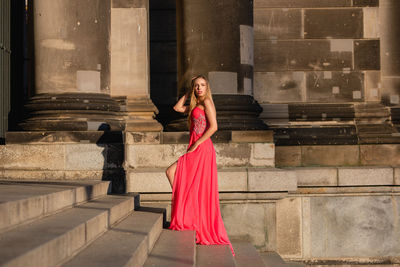 Full length side view of young woman in pink evening gown standing at on steps