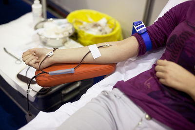 Midsection of woman donating blood while lying in hospital