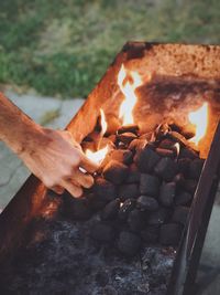 Close-up of hand by burning coals on barbeque grill