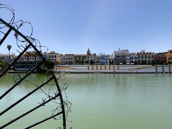 View of buildings by river against clear sky