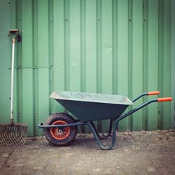 Wheelbarrow and gardening fork by corrugated iron