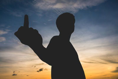 Silhouette man showing obscene gesture against sky during sunset