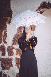 Woman with umbrella standing against brick wall
