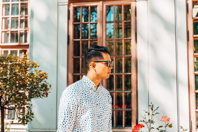 Young man wearing sunglasses while standing against window