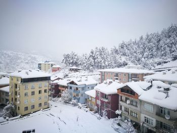 Snow covered houses by buildings against sky