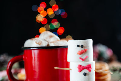 Red enamel mug of hot chocolate with marshmallow snowman on christmas background