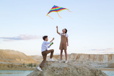 A boy and a girl launch a bright kite in the mountains near the river.