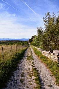 Road passing through field against sky