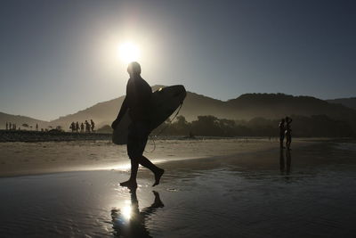 Silhouette men on beach against sky during sunset