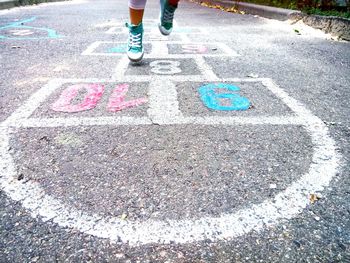 Low section of girl playing hopscotch on road in city