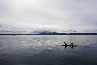 Men sitting on lake against sky