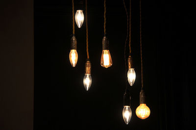 Low angle view of illuminated light bulb hanging against black background