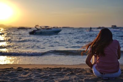 Rear view of woman on beach against sky during sunset