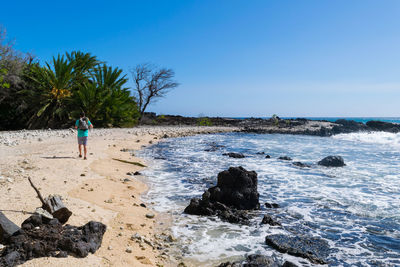 Rear view of man walking at beach against blue sky