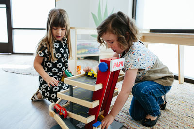 Two young girls play together with wooden cars