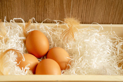 Four brown hen eggs and chicken feather on white shredded paper in wooden basket, top view photo