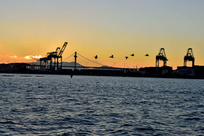 Silhouette cranes at commercial dock against sky during sunset