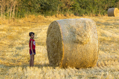 Portrait of girl standing by hay bales on field