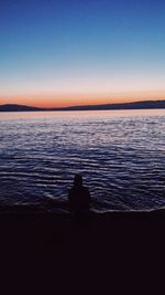 Silhouette of man sitting against sea at sunset