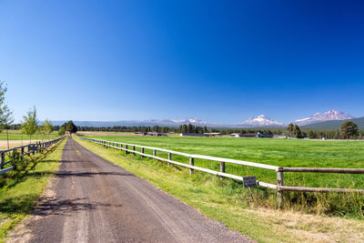 Road amidst field against clear blue sky