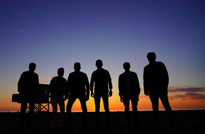 Silhouette people standing on shore against sky during sunset