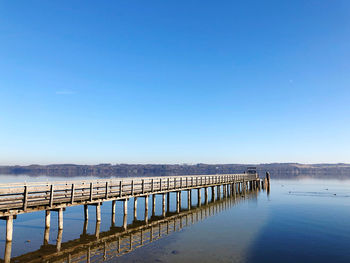 Pier on sea against clear blue sky