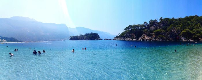 People swimming in sea against clear sky on sunny day