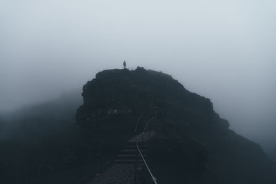 Silhouette man on cliff against sky during foggy weather