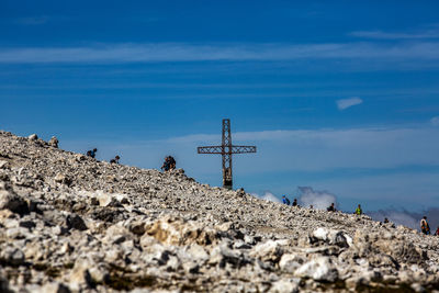 Cross on rocks by sea against blue sky