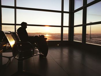 Silhouette mid adult man sitting at airport departure area during sunset