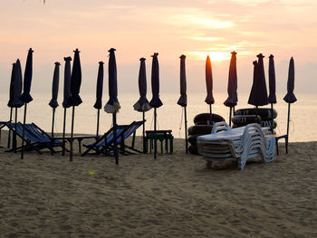 Chairs on wooden posts at beach against sky during sunset