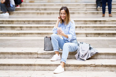 Young woman using phone while sitting on steps