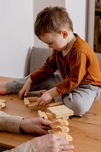 Father and son sitting together at home and playing with wooden blocks. jenga game