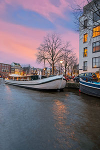 Canal by buildings in city against sky at dusk