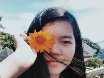 Portrait of woman holding cosmos flower while standing in back yard