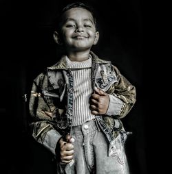 Portrait of smiling boy standing against black background