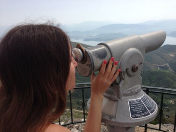 Close-up of woman looking at mountains through coin-operated binoculars