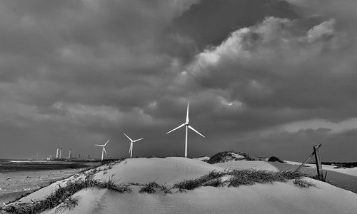 Wind turbines on snowcapped mountain against sky