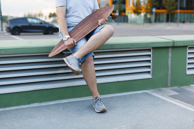 Male in shorts and grey sneakers holding longboard in hands. wooden longboard, urban area