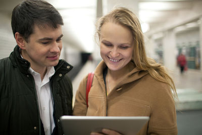 Smiling couple using digital tablet while standing at subway station