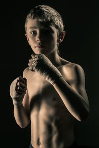 Portrait of boy standing against black background