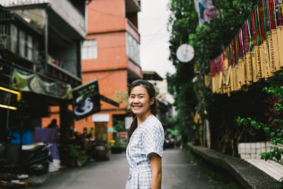 Portrait of smiling young woman standing against buildings in city
