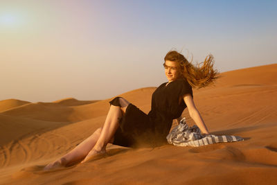 Woman on sand dune in desert against sky