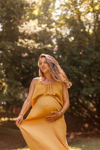 Pregnant woman holding stomach while standing outdoors