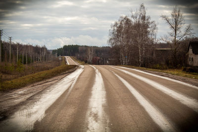 Empty road along bare trees against sky
