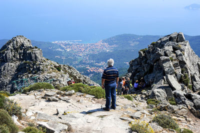 Rear view of man standing on rock by mountain against sky