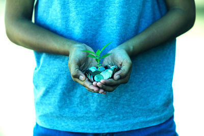 Midsection of man holding seedling and coin