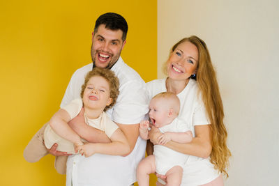 Father and mother stand side by side on a yellow background and hold the brothers' children