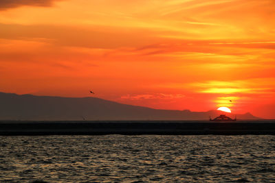 Idyllic shot of sea and silhouette mountains against orange sky