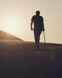 Rear view of silhouette man standing on sand against sky